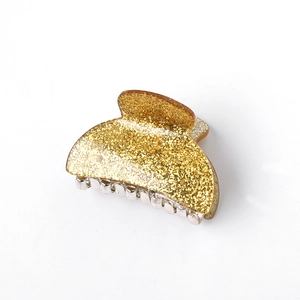 Close-up of golden glitter acrylic hair claw clip with silver metal spring and teeth