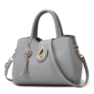Light gray lychee pattern tote bag with golden hardware and tassel charm on white background