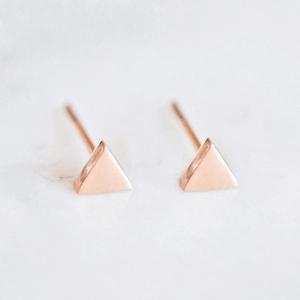 Minimalistische driehoekige oorknopjes in roségoud op witte marmeren achtergrond