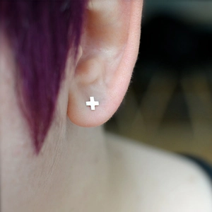 Minimalist silver cross stud earring for women shown on ear in high-quality close-up view