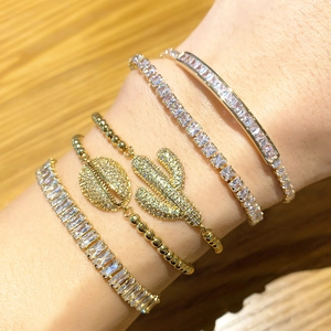 Close-up of stacked gold charm bracelets featuring zircon cactus and shell pendants