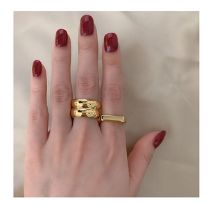 Close-up of three 18K gold-plated wide band rings on finger over champagne silk fabric