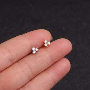 Macro view of mini gold and silver clover stud earrings held to show true small scale