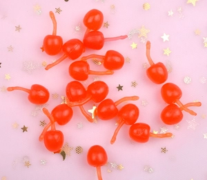 Flat lay of red cherry resin charms for DIY crafts on a pink glittery star background