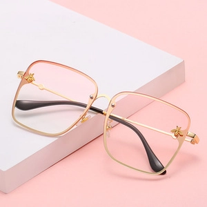 Detail of square metal sunglasses featuring pink gradient lenses and gold bee accents