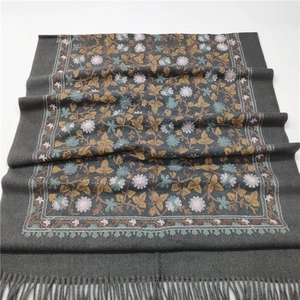 Detailed view of floral embroidery and fringe tassels on a thick grey cashmere-like shawl