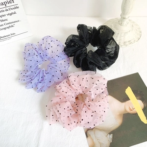 Three oversized polka dot organza scrunchies in purple, black and pink on white fabric