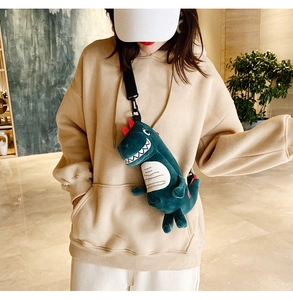 Détail du sac à bandoulière dinosaure en peluche verte porté par un mannequin en intérieur