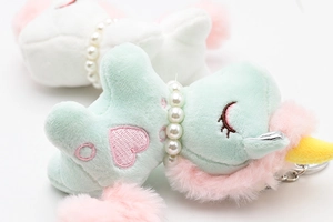 Close-up of green plush unicorn keychain with pearl necklace and heart embroidery