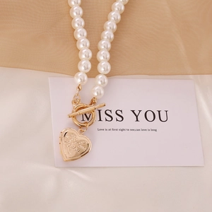 Gold heart locket pearl necklace with toggle clasp on beige silk fabric background