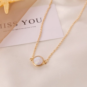Close-up of a gold semi-precious stone necklace with a round white opal pendant on silk