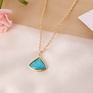 Collar dorado con colgante de piedra semipreciosa azul en forma de abanico sobre seda