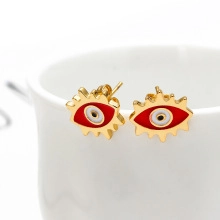 Detailed close-up of golden evil eye stud earrings with red and white enamel accents
