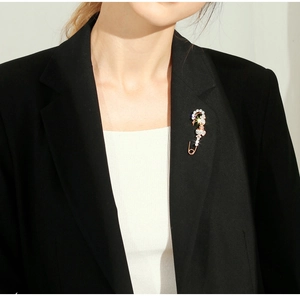 Macro view of a large gold safety pin brooch with white crystals on a black suit lapel