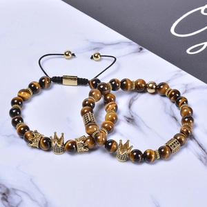 Macro shot of 8mm tiger eye beads with gold crown charm and zircon inlay on marble