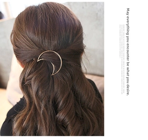 Detail of a minimalist gold moon-shaped metal barrette worn on wavy brown hair