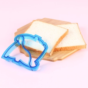 Blue house-shaped plastic sandwich cutter placed on a wooden board with toast bread slices