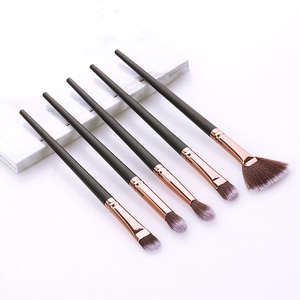 Detail view of five makeup brushes with rose gold ferrules on white marble background