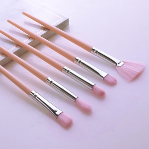 Detailed view of five pink makeup brushes with silver ferrules on a white surface