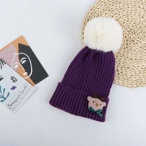 Détail du bonnet de Noël en tricot violet avec pompon en fausse fourrure et écusson cerf