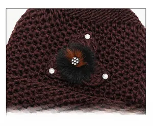 Close-up of deep wine red knitted hat featuring a faux fur pompom and rhinestone accents