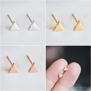 Macro detail of tiny geometric triangle stud earrings in silver, gold, and rose gold