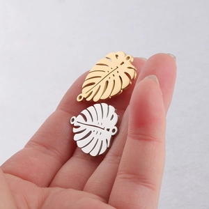 Polished gold and silver monstera leaf pendants held to show fine metal texture