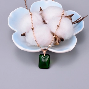 Detailed close-up of emerald green rectangular zircon pendant on rose gold beaded chain