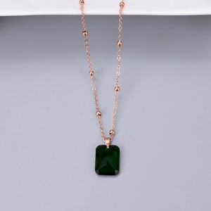Macro detail of rose gold beaded chain with emerald green rectangle cut pendant
