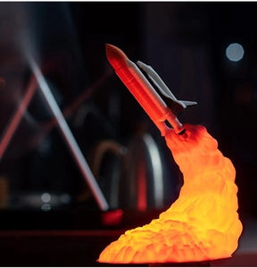 Close-up of a 3D printed space shuttle lamp with glowing orange rocket flame base
