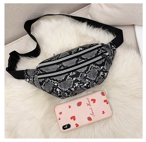 Close-up of snakeskin fanny pack with double zippers on a white plush background