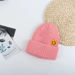 Dettaglio del berretto in maglia rosa con patch gialla ricamata a forma di smiley