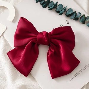 Close-up of a large wine red satin bow hair clip on a minimalist white background