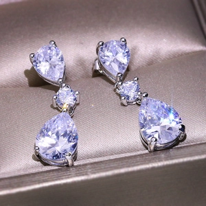 Macro shot of silver teardrop zircon earrings on a champagne velvet jewelry box
