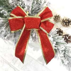 Macro detail of red glitter Christmas bow with gold edges on snowy pine branch