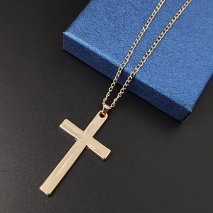 Detail view of a minimalist gold cross pendant necklace resting on a blue textured gift box