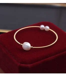 Macro shot of gold wire-wrapped freshwater pearl open cuff bracelet on red velvet