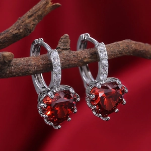 Macro shot of heart-shaped red zircon earrings with diamond accents on a silver base
