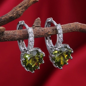 Detail of silver heart earrings with green zircon stones hanging on a dark wood branch