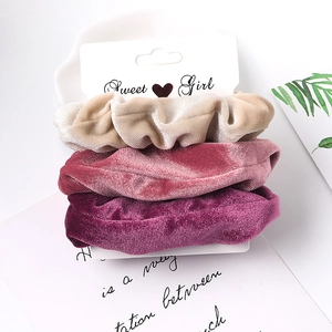 Close-up of three velvet hair scrunchies in beige, pink and purple on a white display card
