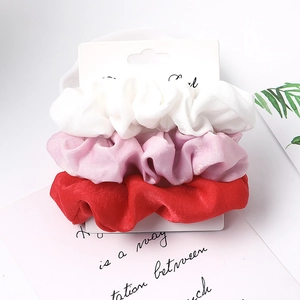 Three-piece set of satin fabric scrunchies in white, pink and red on a display card