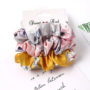Close-up of three floral satin scrunchies in gray, pink, and yellow with silk texture
