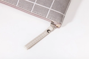 Close-up of grey plaid fabric makeup bag with durable zipper and metal rivet detail