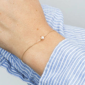 Detail of a minimalist silver chain bracelet with a round white pearl on a wrist
