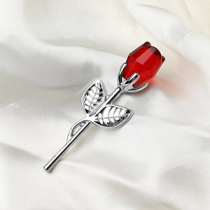 Macro shot of red crystal rose brooch with silver metal leaves on white silk fabric