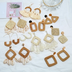 Flat lay of handmade Bohemian woven earrings with shell and tassel details on white surface
