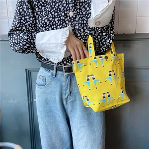 Close-up of yellow canvas tote bag featuring cute cartoon character prints and top handles