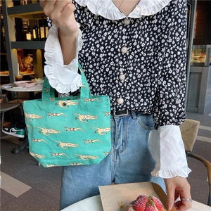 Green canvas lunch tote bag featuring a repeating swimmer pattern in a cafe setting