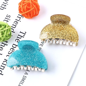 Flat lay of two glittery acrylic claw clips in gold and blue with decorative yarn props