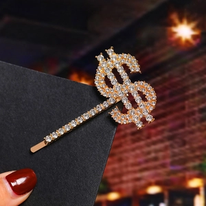 Macro shot of gold dollar sign hair clip with sparkling rhinestones on black card